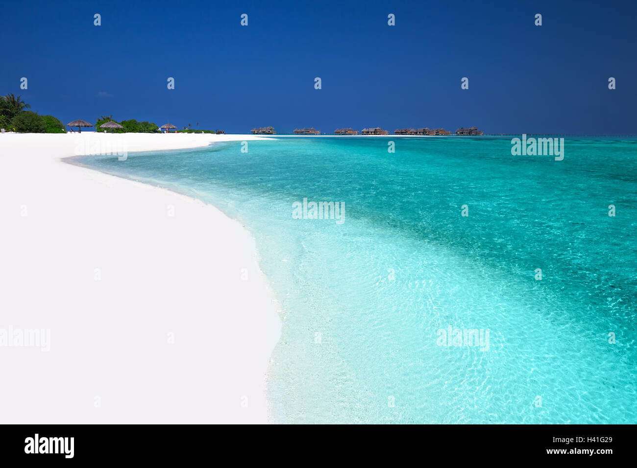 Tropical island with sandy beach, palm trees, overwater bungalows and turquoise clear water Stock Photo