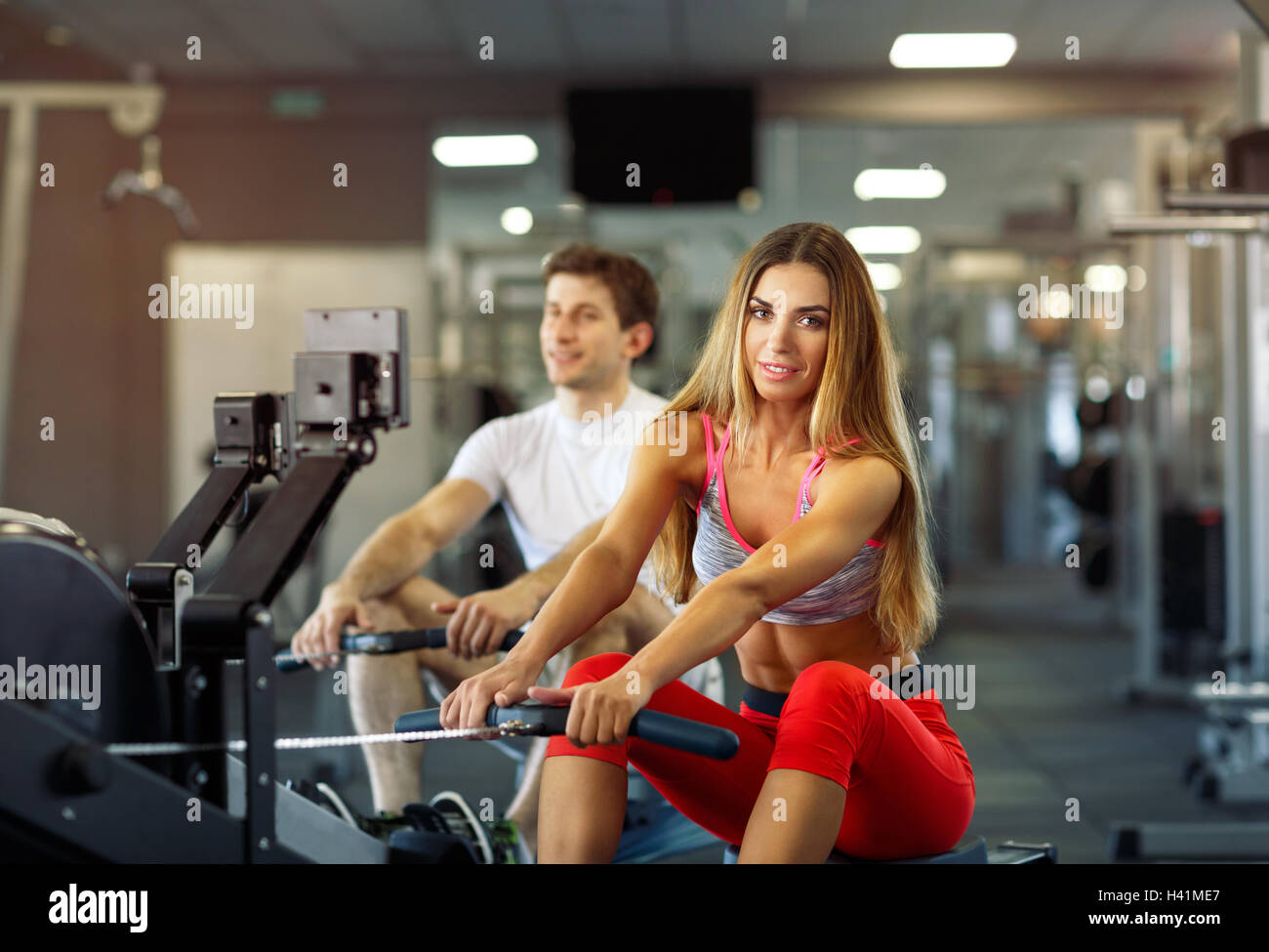 Athletic couple - man and woman training on row machine in gym Stock Photo