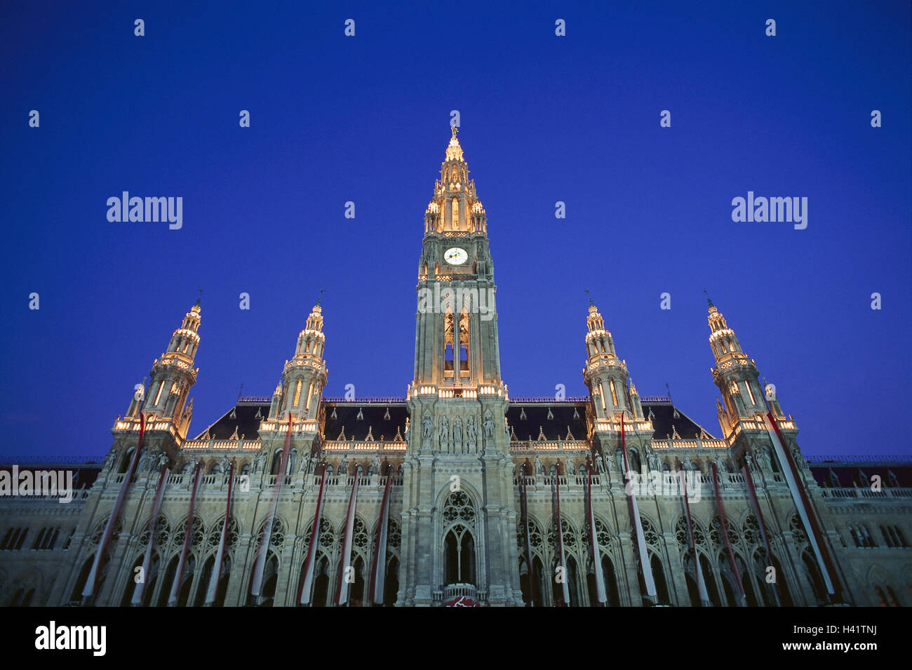 Austria, Vienna, city hall, lighting, evening, from below, Europe, capital, city hall building, structure, in 1872-83, builder Friedrich von Schmidt, architectural style, architecture, new Gothic, tower height 97.9 m, facade, flags, national flags, flags, landmarks, place of interest, culture, perspective, splendour construction, wealth, power, incredibly, imposingly, rule, impressively, night Stock Photo