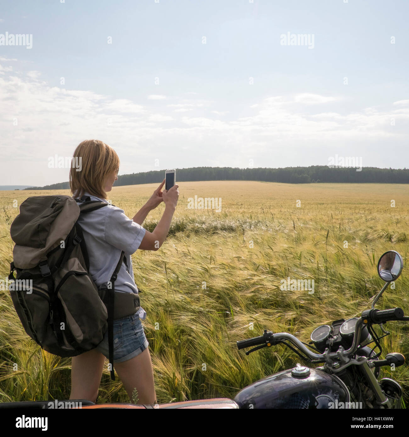 Caucasian woman standing in field near motorcycle using cell phone Stock Photo