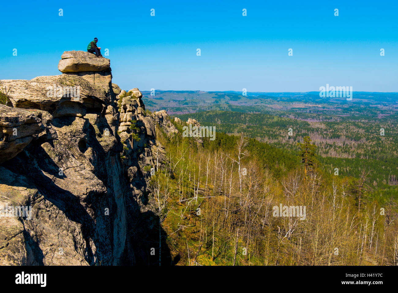Caucasian man sitting on mountain rock admiring scenic view Stock Photo