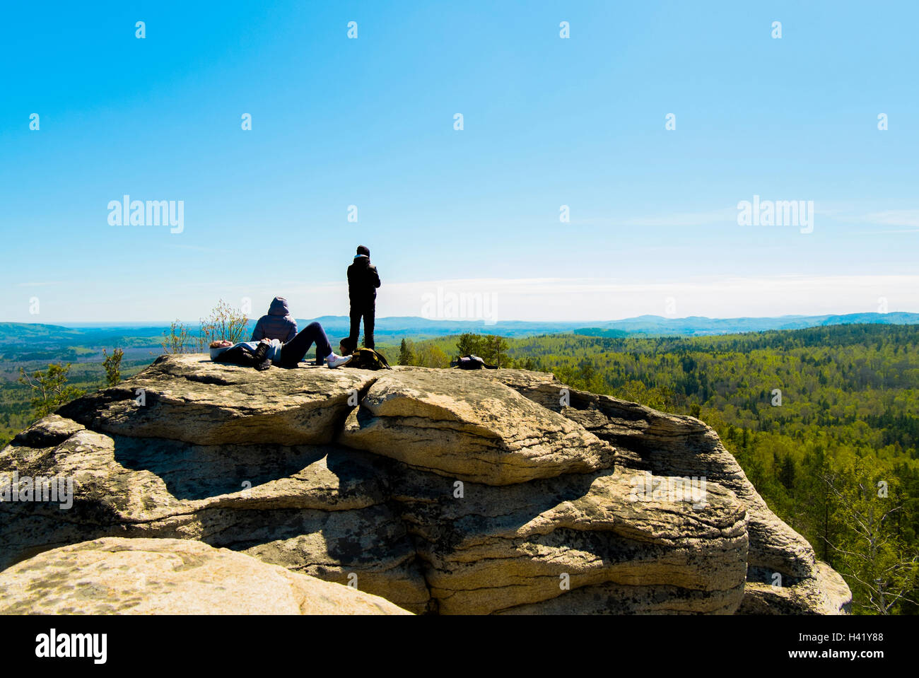 Caucasian friends sitting on mountain rock admiring scenic view Stock Photo