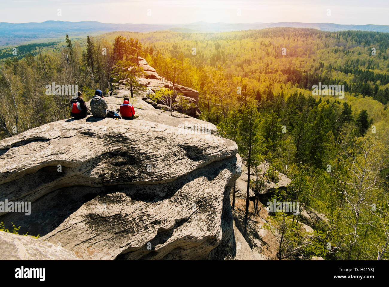 Caucasian friends sitting on mountain rock admiring scenic view Stock Photo
