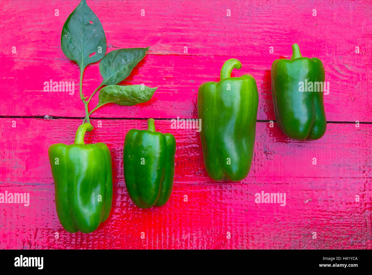 Close up of row of green peppers on red wooden table Stock Photo - Alamy