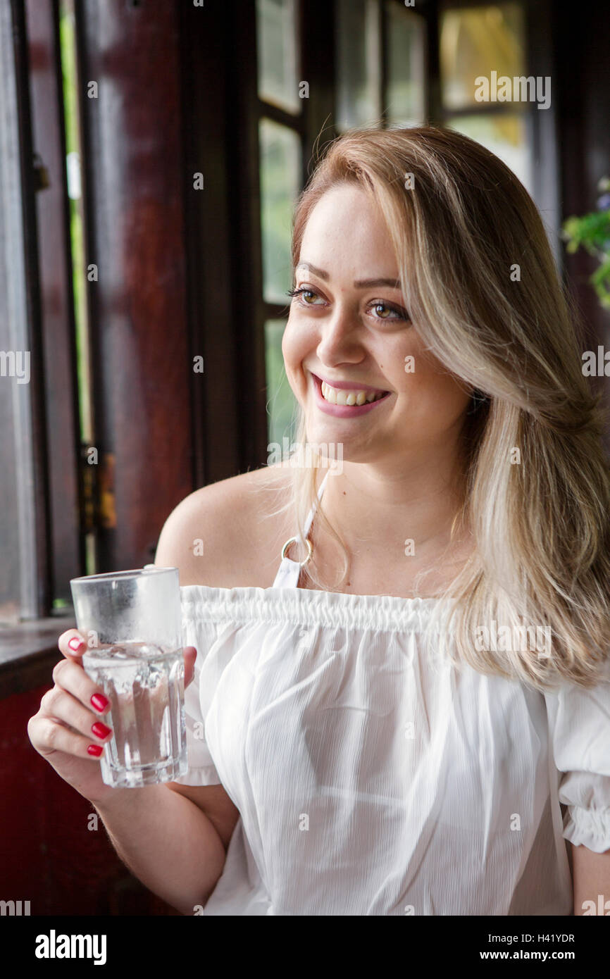 Smiling Hispanic woman drinking glass of water near window Stock Photo