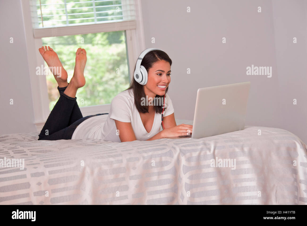 Hispanic woman laying on bed listening to laptop with headphones Stock ...