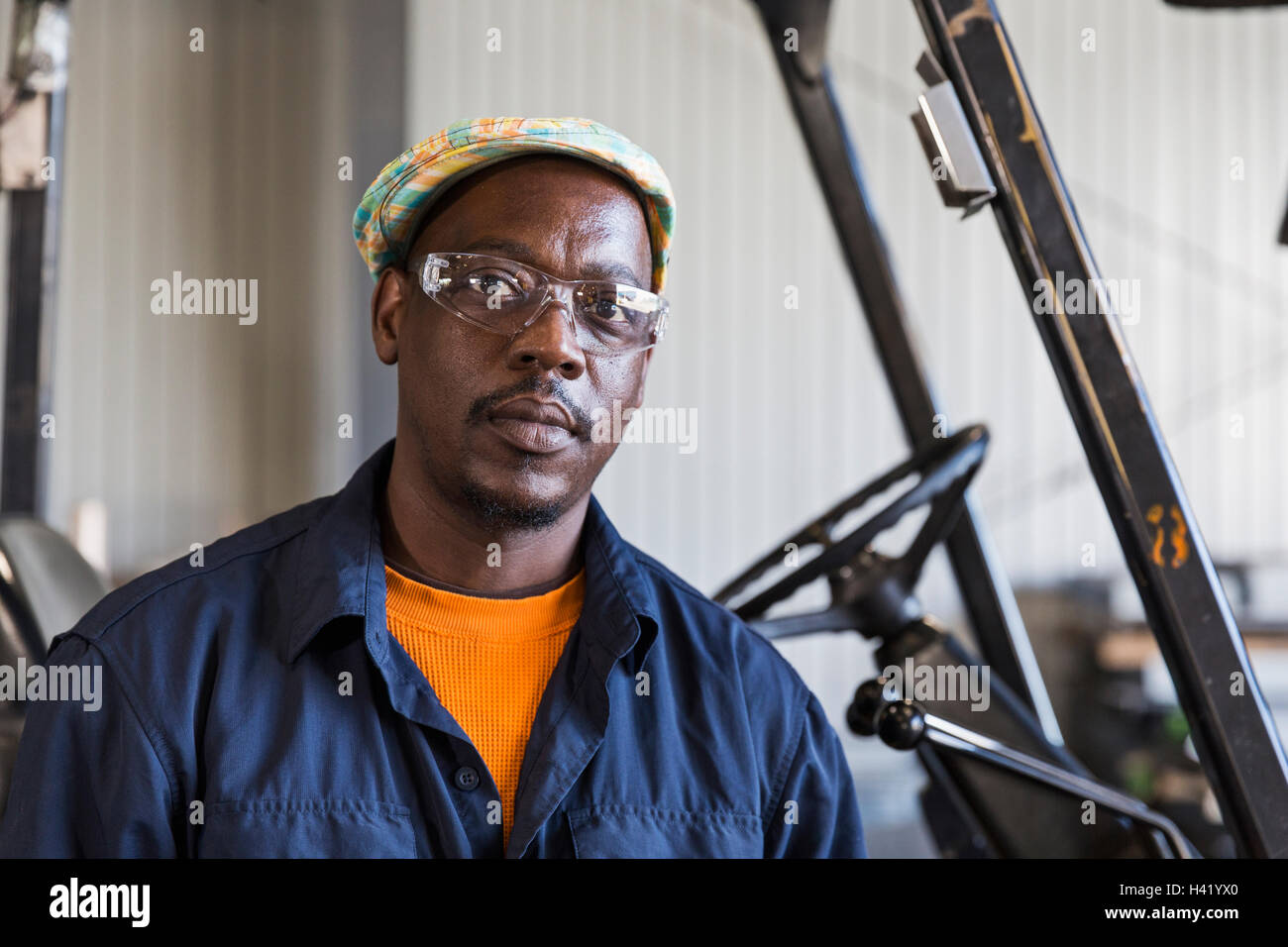 Serious Black worker posing near forklift in factory Stock Photo
