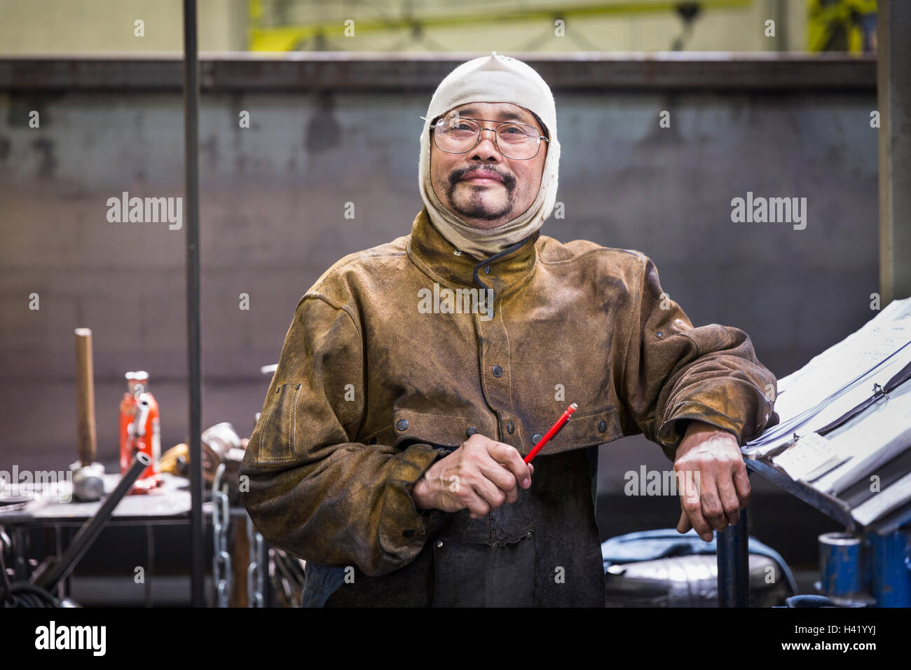 Smiling Asian worker wearing hood posing in factory Stock Photo