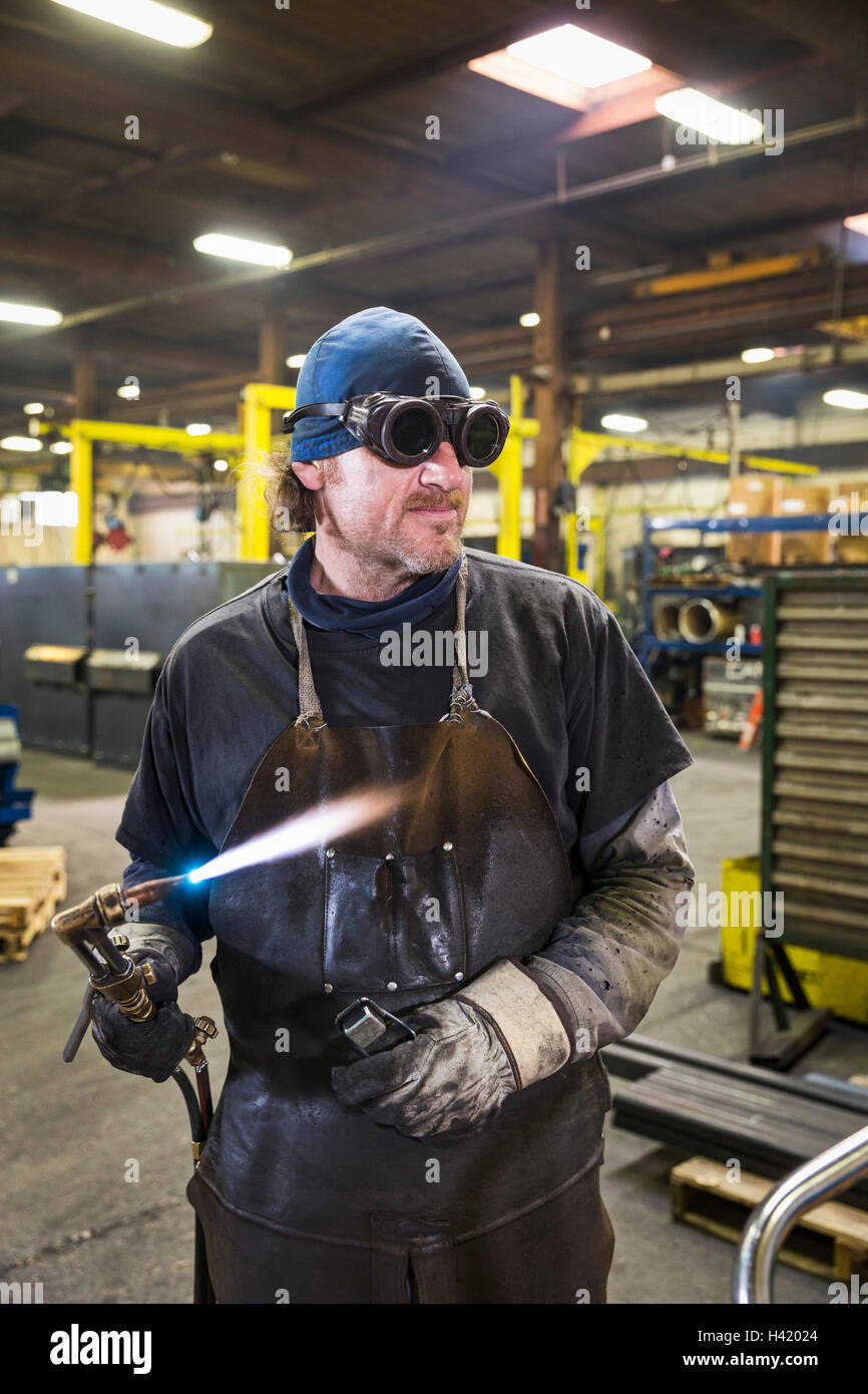 Caucasian welder holding  blowtorch in factory Stock Photo