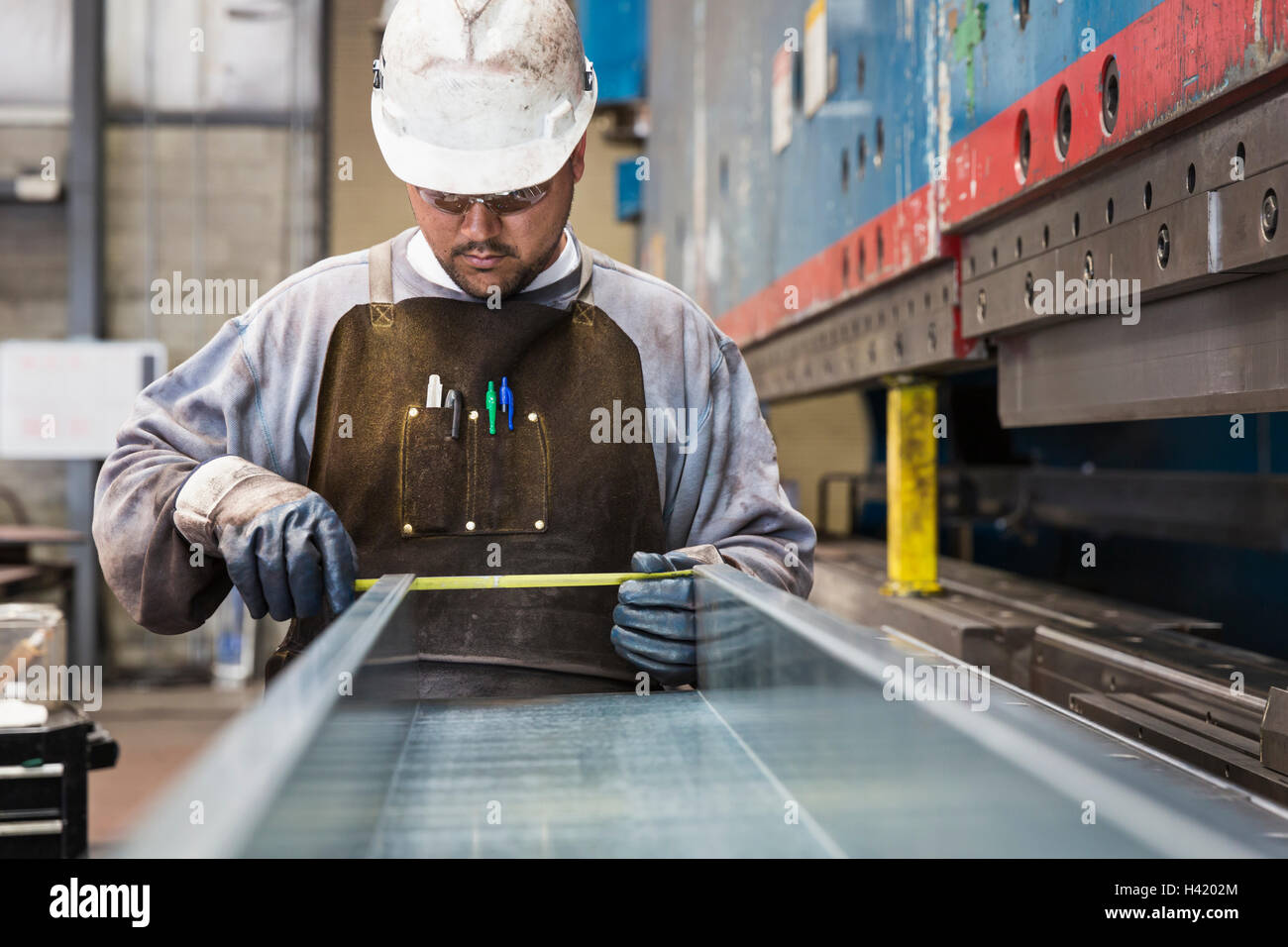 Pacific Islander worker measuring metal in factory Stock Photo