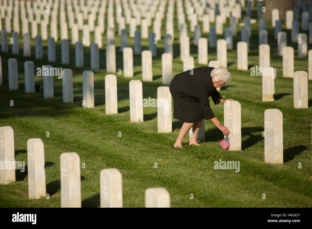 Caucasian widow placing American flag at cemetery gravestone Stock Photo