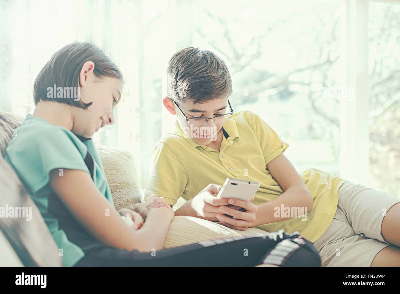 Mixed Race brother and sister texting on cell phone near window Stock Photo