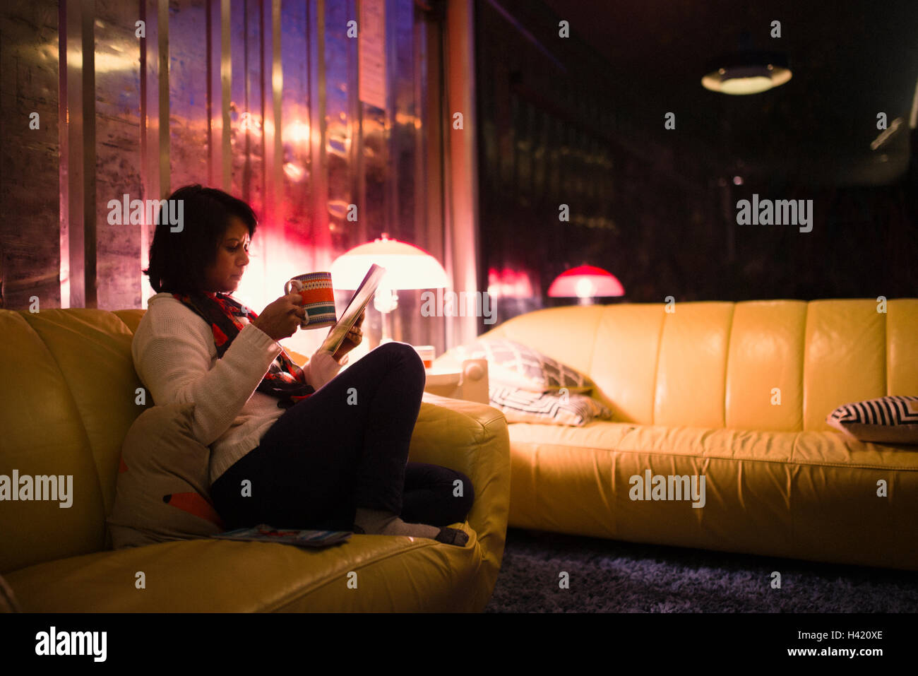 Woman drinking tea and reading magazine on sofa Stock Photo