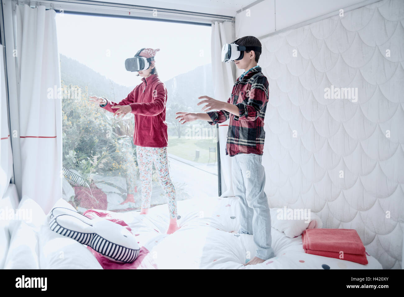 Mixed Race brother and sister using virtual reality goggles on bed Stock Photo