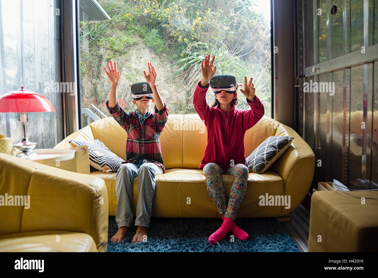 Mixed Race brother and sister using virtual reality goggles on sofa Stock Photo