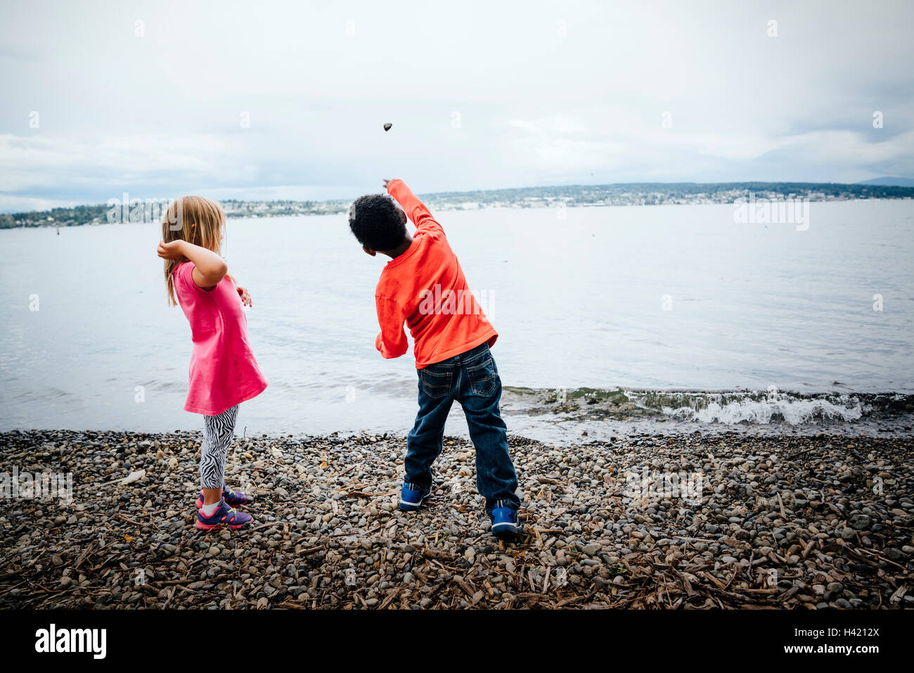 Boy and girl throwing rocks into river Stock Photo