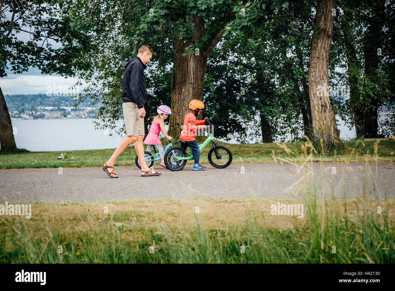 Father watching daughter and son riding bicycles Stock Photo