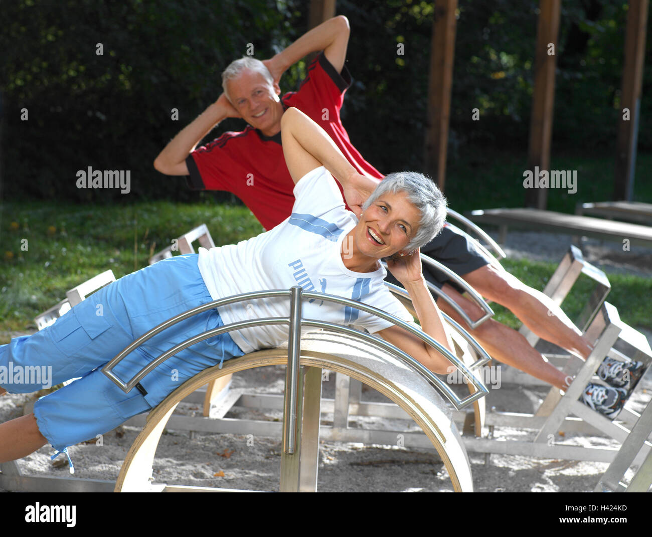Trimm-dich-Pfad, senior citizens, training device, lie at the side, exercises, abdominal musculature 50-60 years, couple, sportily, sport, activity, gymnastics, gymnastics exercises, gymnastics practise, health, fitness, training, musculature, strengthening, stomach muscles, abdominal muscle training, rationalisation, consolidation, practise, laugh, happily, cheerfulness, together, leisure time, hobby, activity, edge of the forest Stock Photo