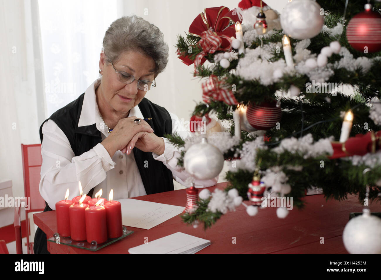 Christmas, senior, letter  writes, thoughtful  sitting woman, 50-60 years, 60-70 years, glasses, table, stationery, Christmas mail letter letters thoughts, well, Christmas tree detail candles, candlelight, flames, coziness, silence, silence, thoughtfulness, pre-Christmas period, Christmas time, Advent season, christmassy Stock Photo
