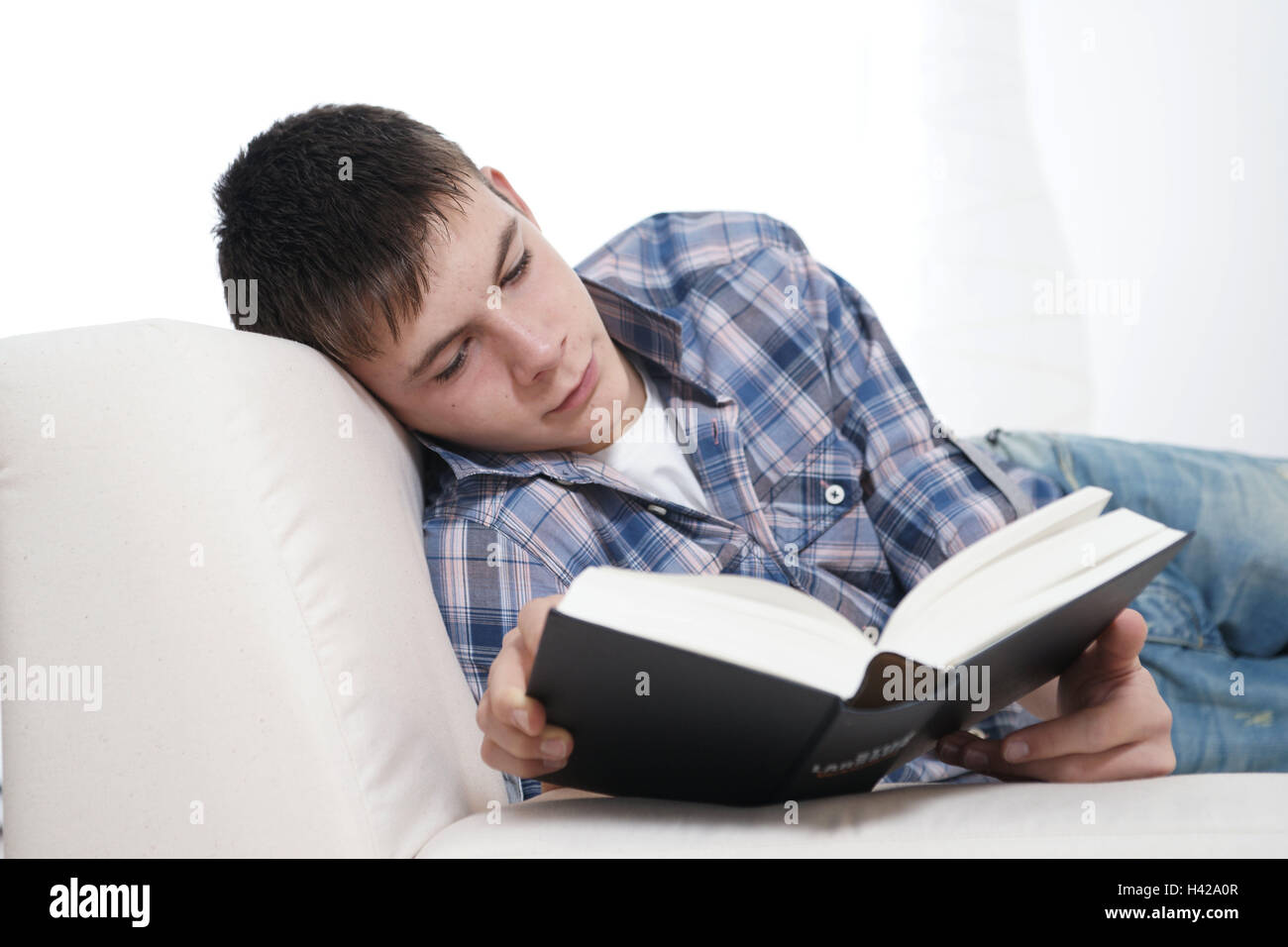 Teenager, boy, lying, sofa, reading, sidewise, model released, Stock Photo