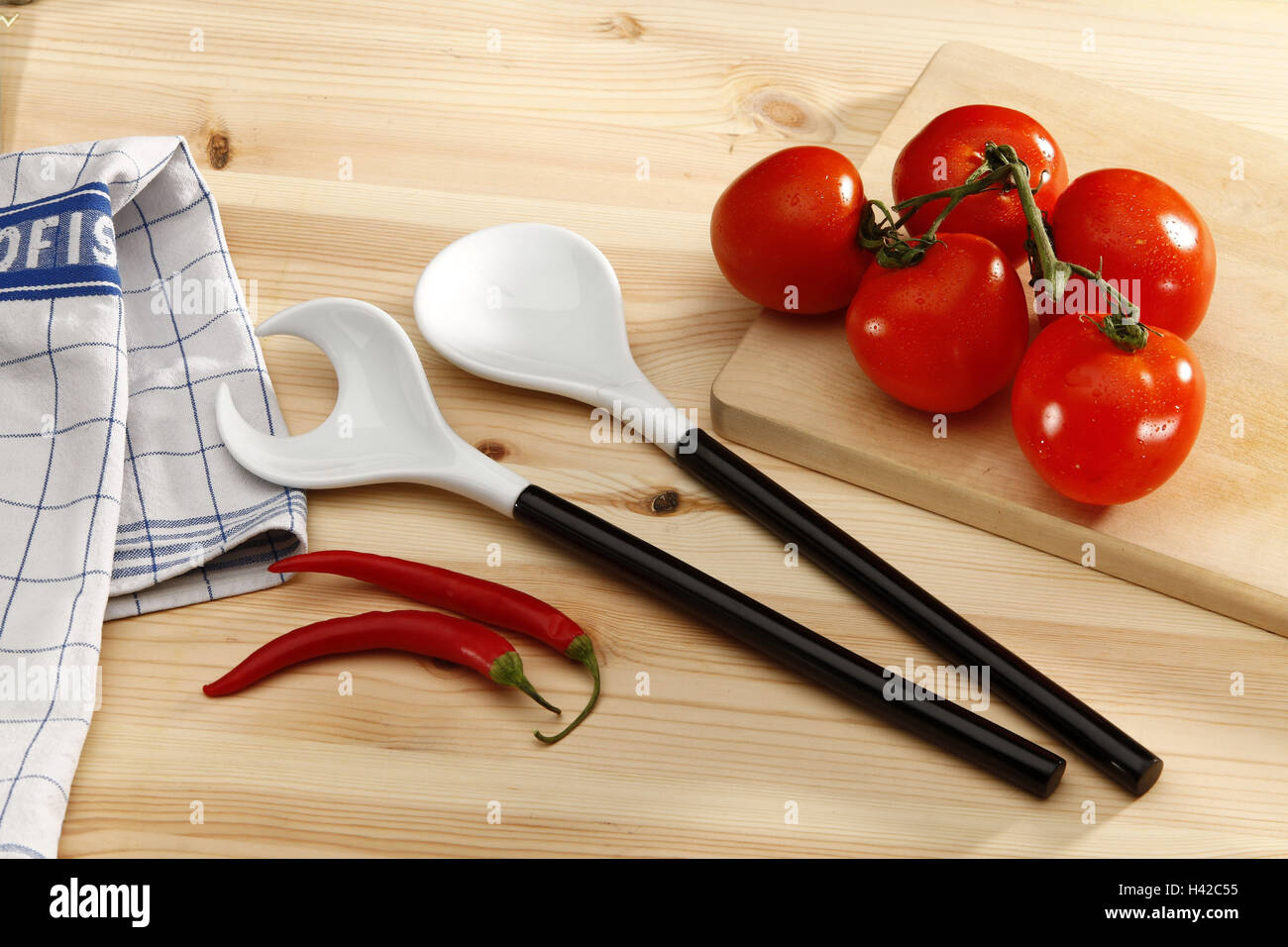 Kitchen table with salad servers, tomatoes, chilli, Stock Photo