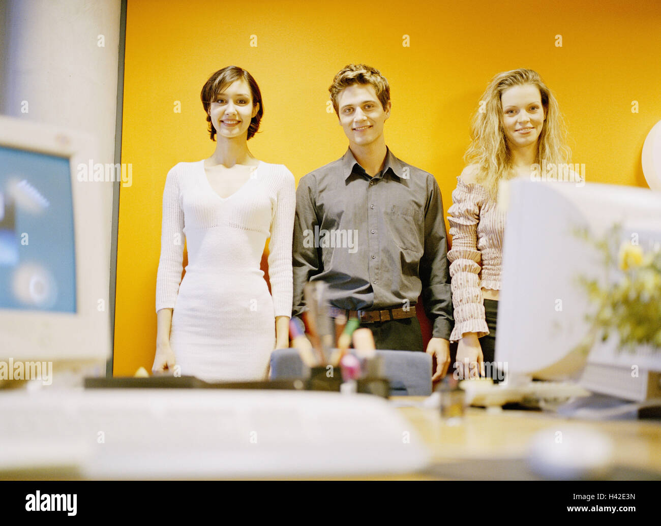 Desk, colleague, stand, smile side by side, view camera, business, office, occupation, workplace, women, man, colleague, teamwork, clerks, business people, together, contently, pleased, success, readiness for action, motivates, readily, service, orange Stock Photo