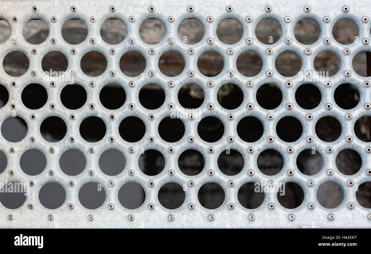 Gray metal grate with round holes and rivets against blurred background. Stock Photo