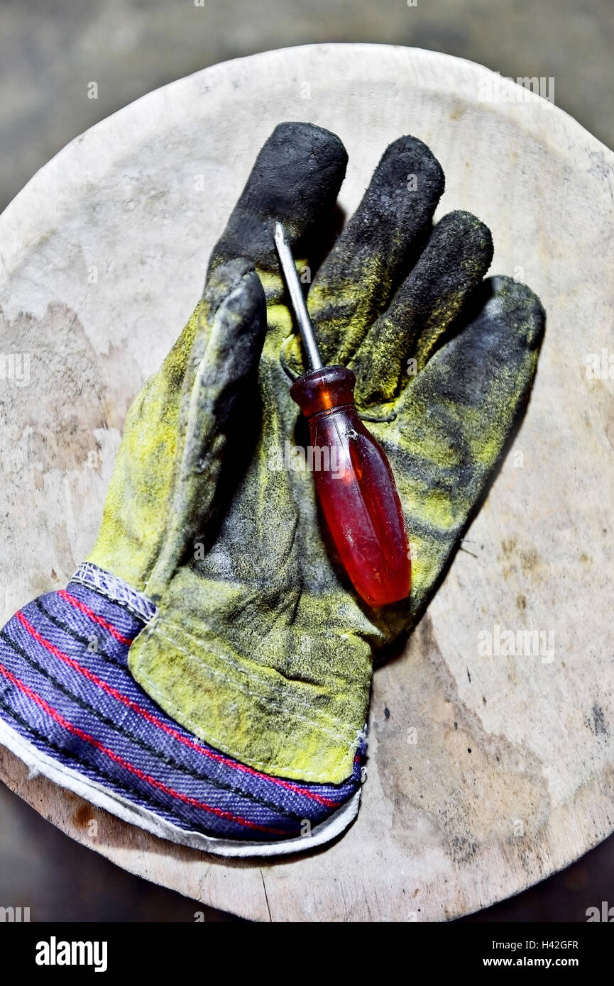 Dirty worker's glove holding a screwdriver on a wooden plank in a workshop Stock Photo