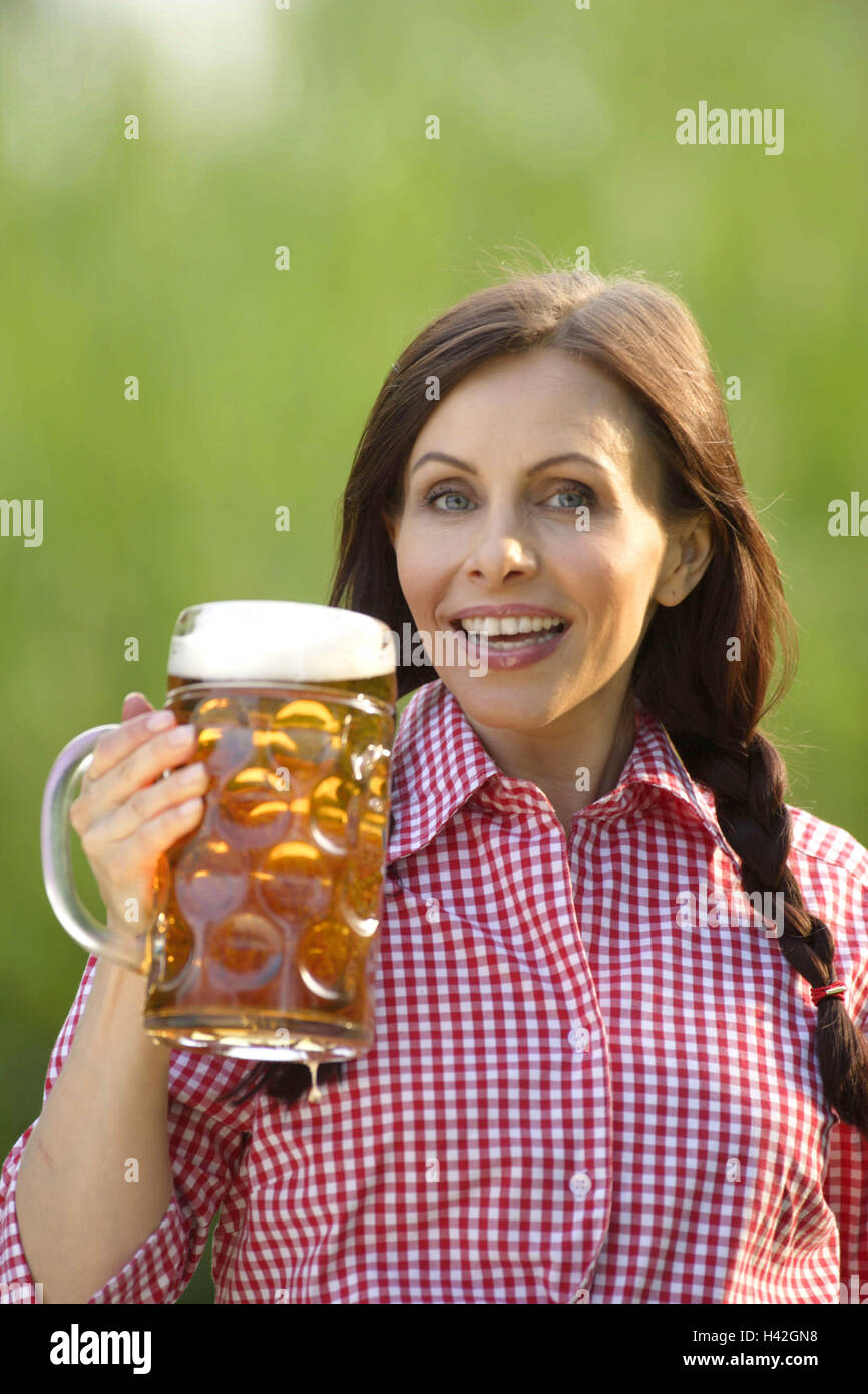 Woman, young, stein, smiles beer,  holds, portrait  Series, women portrait, 30-40 years, gaze camera long-haired, brunette braids shirt blouse, checkered, jug, beer mug, measurement, red-knows drinks, beverage, alcohol, alcoholic, happiness, fun, summers, outside, concept beer garden Lifestyle, competent, hard-drinking, background green Stock Photo