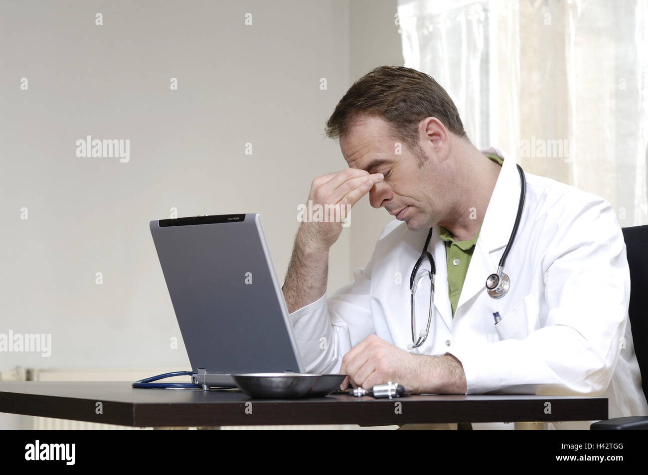 Doctor, desk, laptop, gesture, cephalalgias, half portrait, person, man, medicine, health, disease, public health, practise, medical practise, office, administration, work, occupation, remedial occupation, stethoscope, computer, touch, pains, overfatigue, reworks, Stock Photo