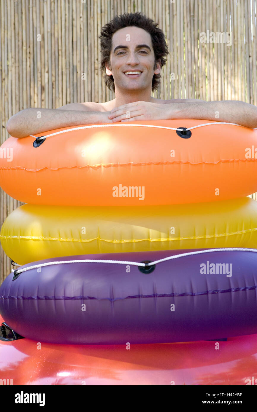 Man, smiles, stands, swimming tires,  stacked, portrait  Men's portrait, 28 years, 20-30 years, dark-haired, gaze camera, happiness, foolishly, fun, summers, outside, swimming rings, inflatable, colorfully, background Strohmatte, concept, leisure time, va Stock Photo