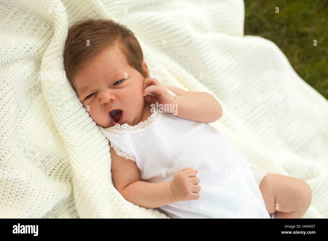 Baby yawing on the blanket on the grass Stock Photo