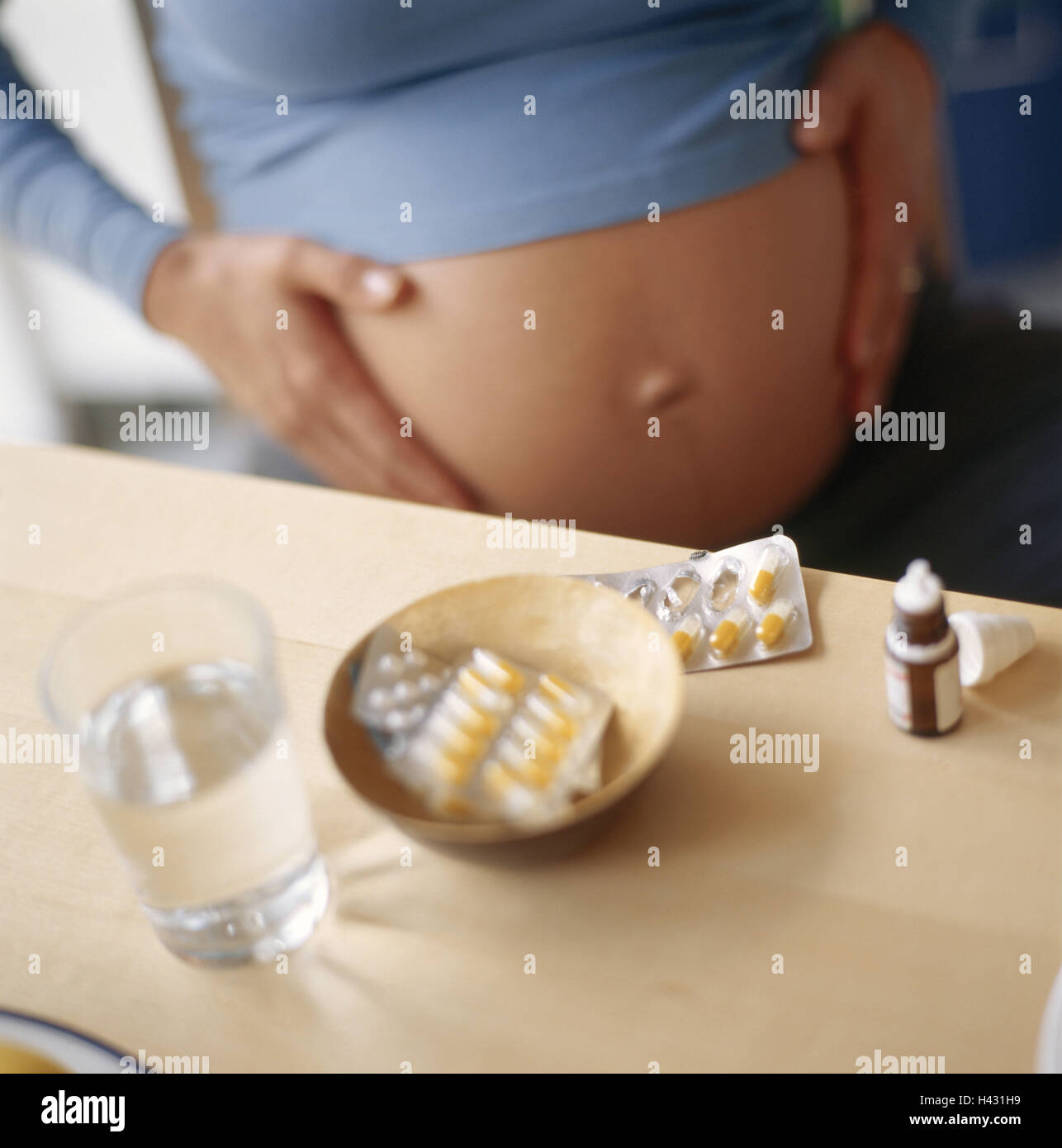 Woman, pregnant, sit, hands, touch, abdomen, table, drugs, capsules