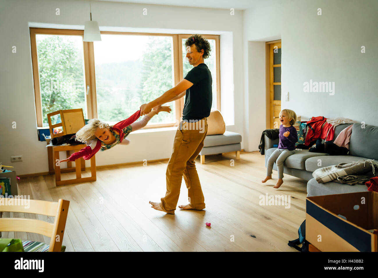 Caucasian father spinning daughter by arm and leg in livingroom Stock Photo