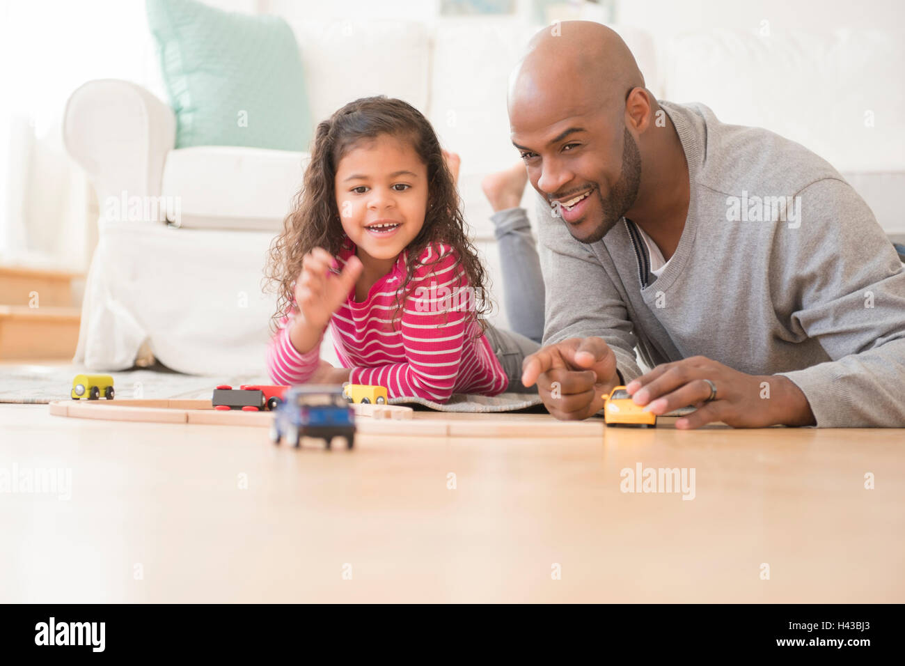 Father and daughter playing with toy cars on floor Stock Photo