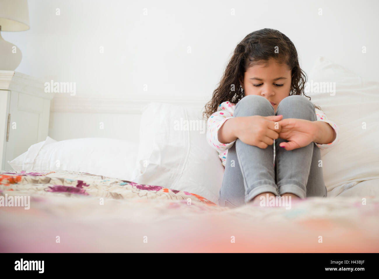 Unhappy Mixed Race girl sitting on bed Stock Photo