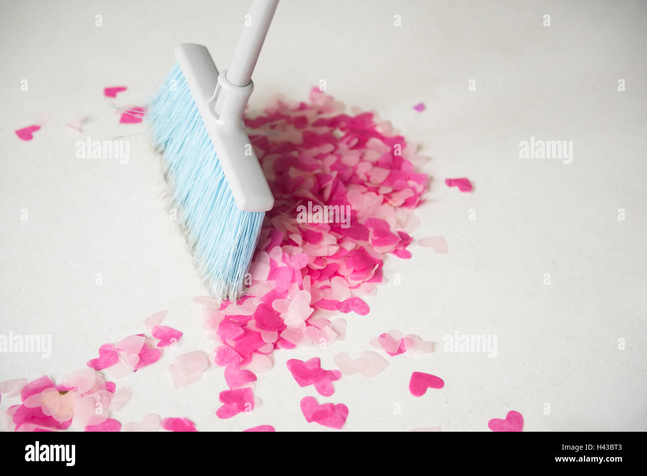 Broom sweeping heart-shape confetti on floor Stock Photo