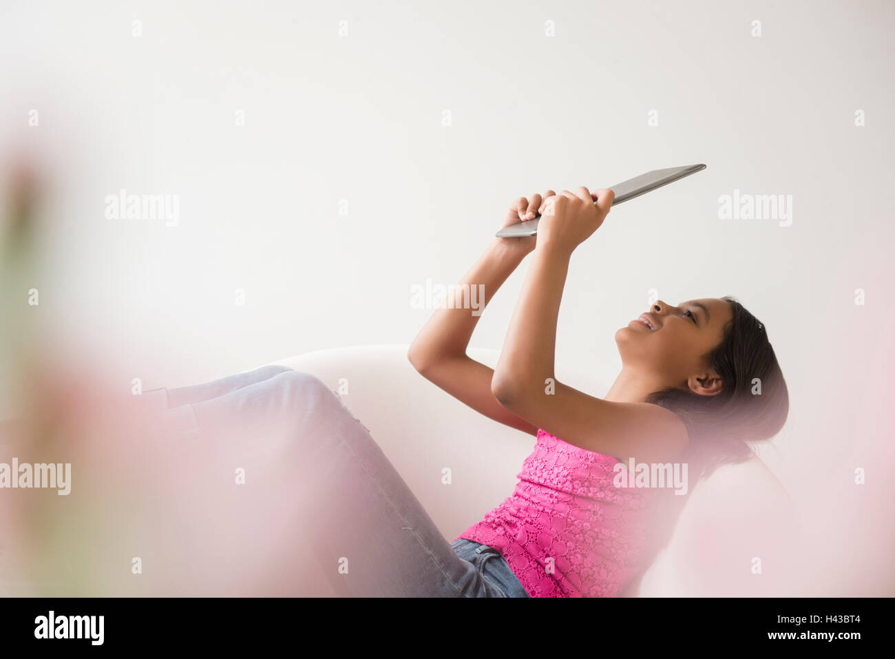 Mixed Race girl relaxing in armchair using digital tablet Stock Photo