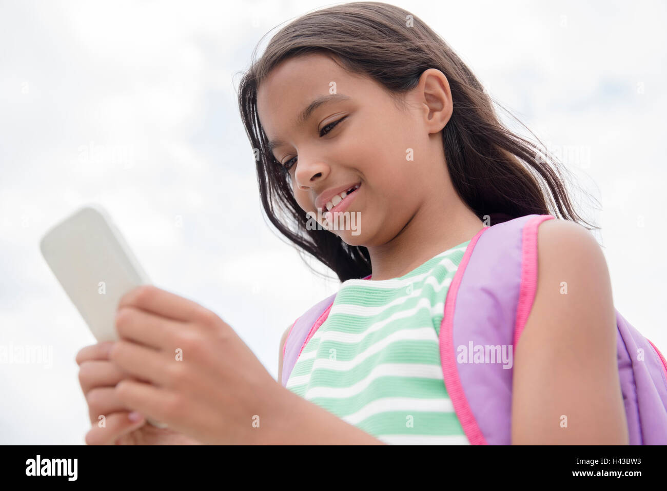 Mixed Race girl carrying backpack texting on cell phone Stock Photo