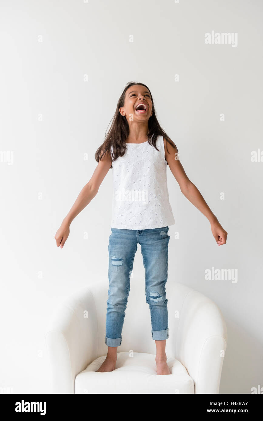 Mixed Race girl standing barefoot on armchair and shouting Stock Photo