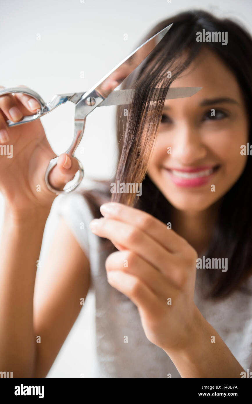 Mixed Race woman cutting hair with scissors Stock Photo