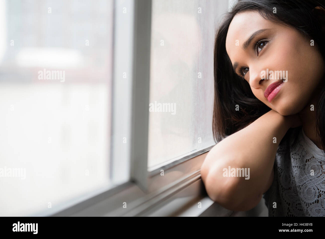 Mixed Race woman daydreaming at window Stock Photo