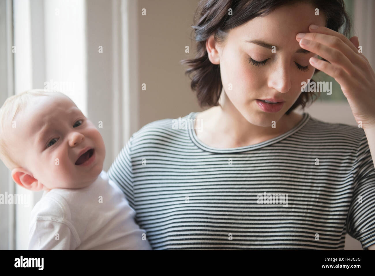 Caucasian mother rubbing forehead while holding baby son Stock Photo
