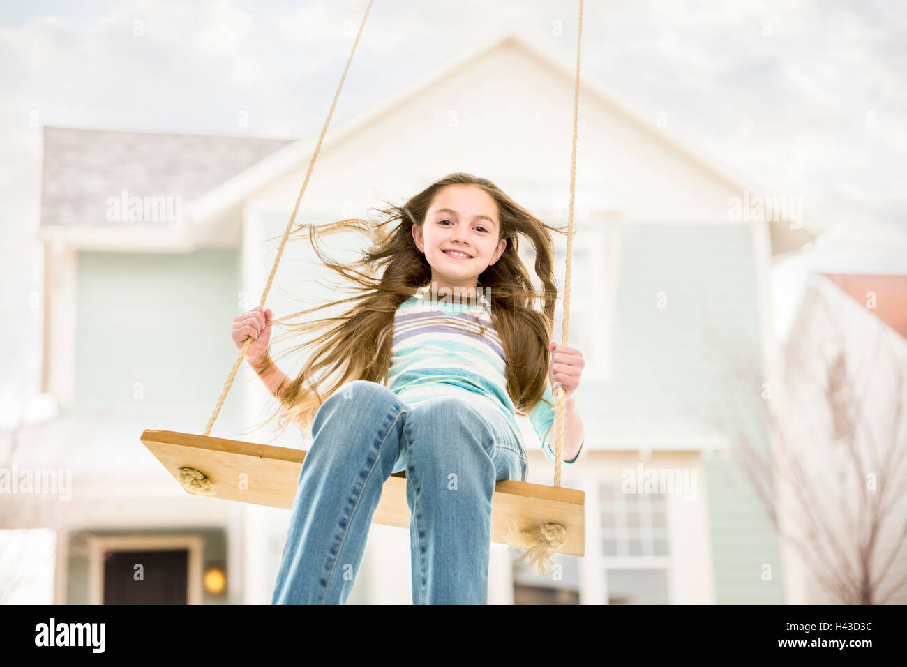 Caucasian girl on rope swing near house Stock Photo