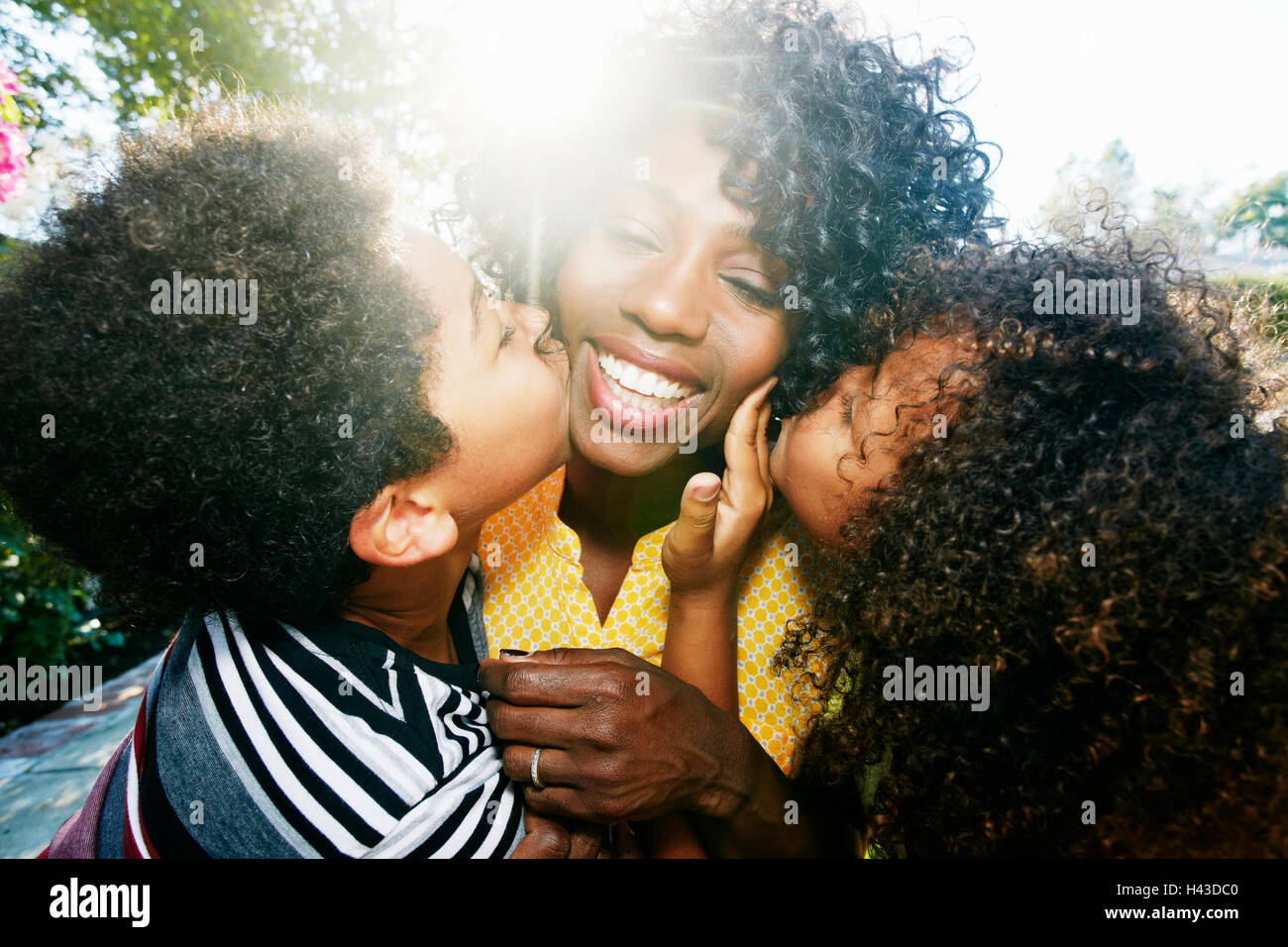Son and daughter kissing cheeks of mother outdoors Stock Photo