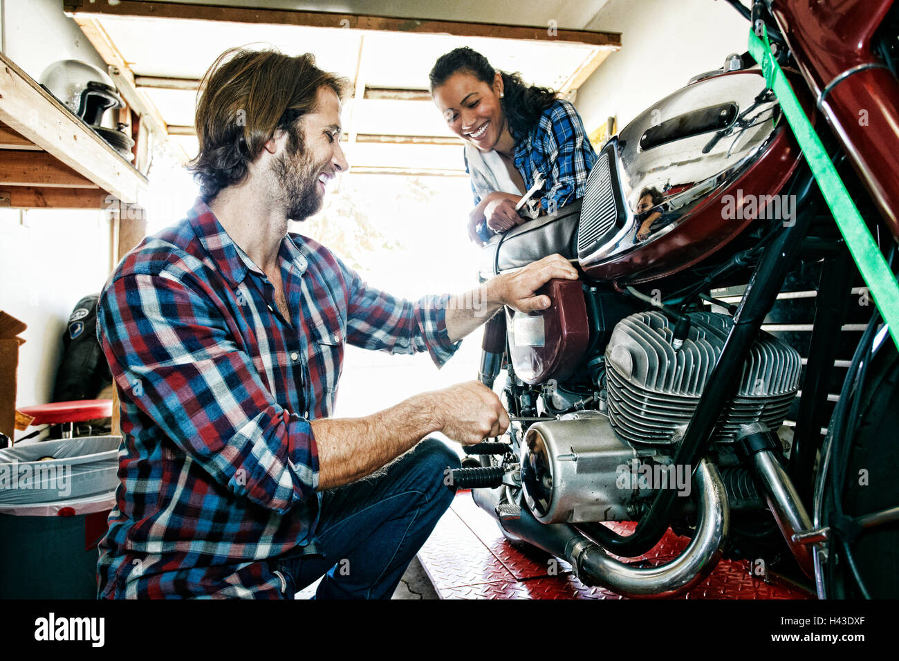 Woman watching man repairing motorcycle in garage Stock Photo