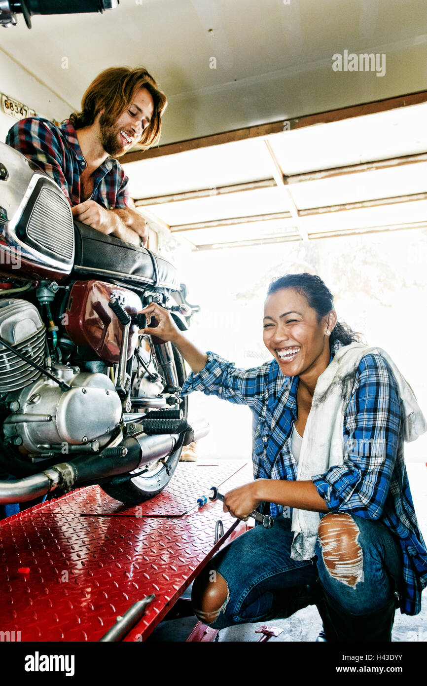 Man watching laughing woman repairing motorcycle in garage Stock Photo
