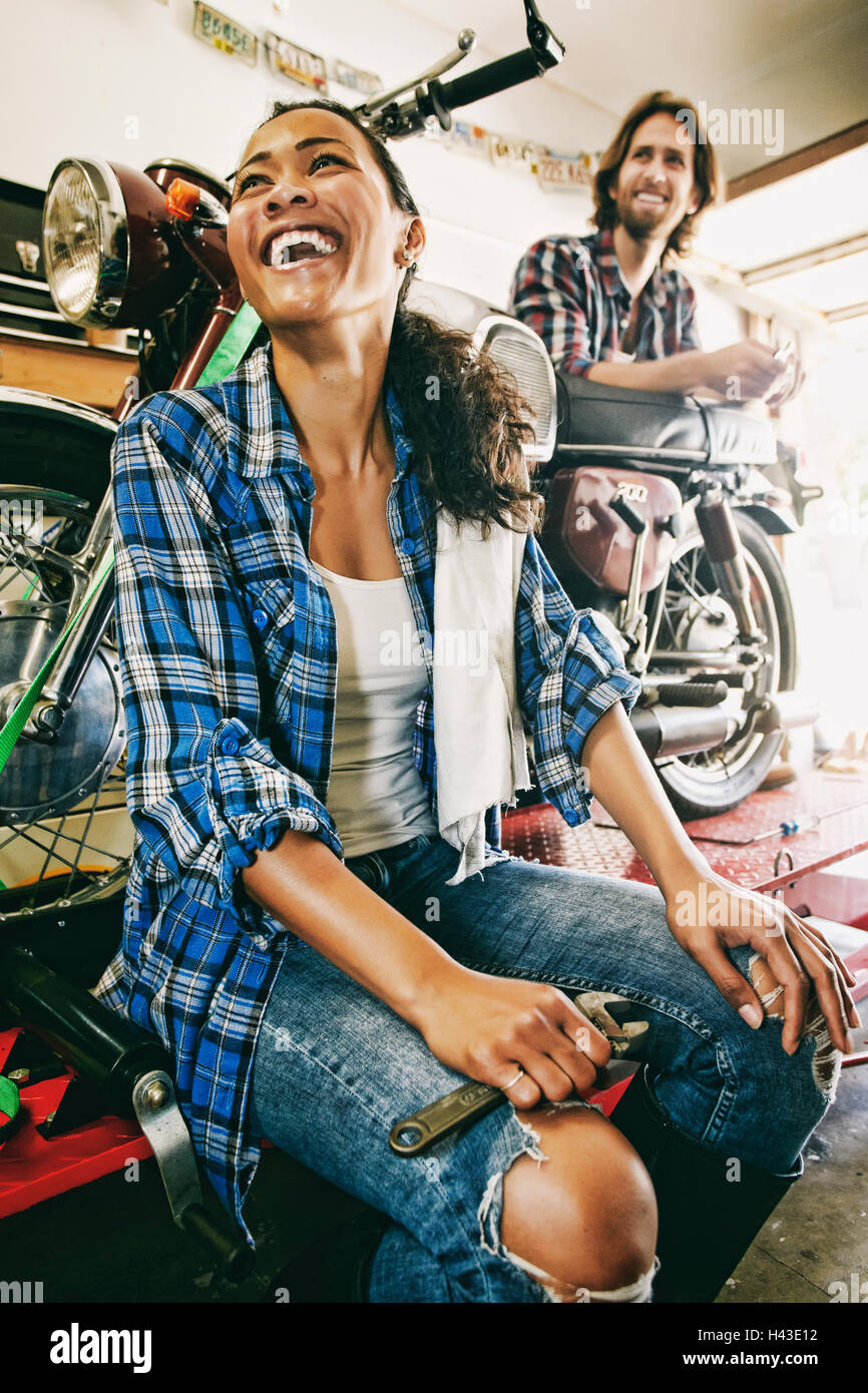 Laughing man and woman repairing motorcycle in garage Stock Photo
