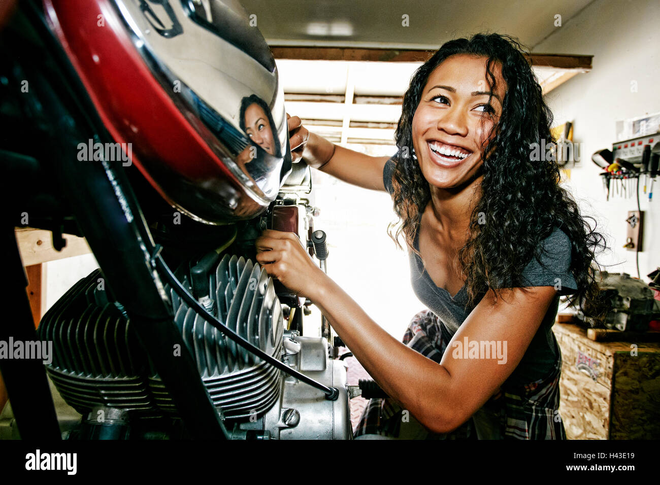 Laughing Mixed Race woman repairing motorcycle in garage Stock Photo