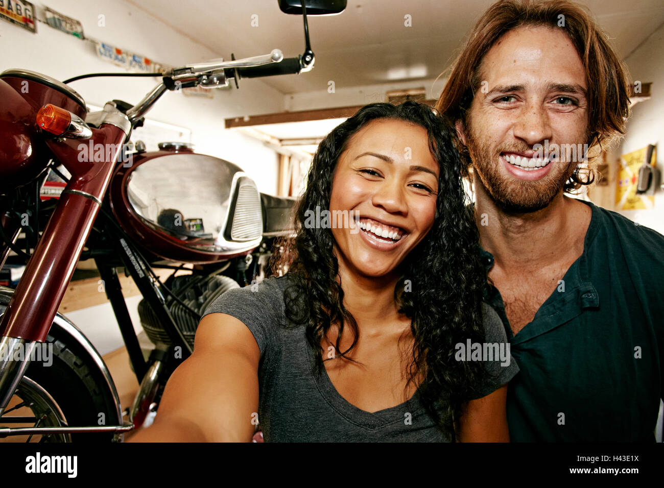 Man and woman posing for selfie with motorcycle in garage Stock Photo